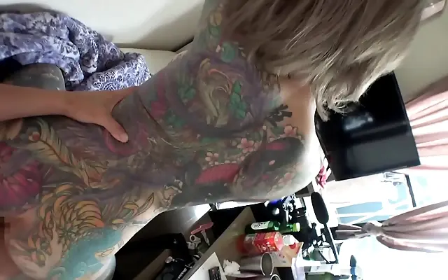 Inked thighs part as she leans in, tattoos swirling down her spine